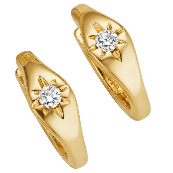 A pair of yellow gold huggie rings, each featuring a central round-cut diamond set in a starburst or sunburst motif with gold rays, shown on a light gray reflective background.